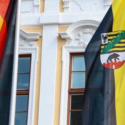 Deutschland- und Landesfahne von Sachsen-Anhalt vor der gelb-weißen Fassades des Landtags von Sachsen-Anhalt am Domplatz in Magdeburg.