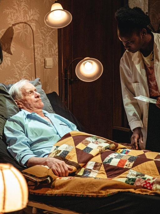 Szene aus dem Stück "Grief & Beauty" von Milo Rau: Ein alter Mann liegt in einem Krankenbett, neben ihm ist eine Pflegerin