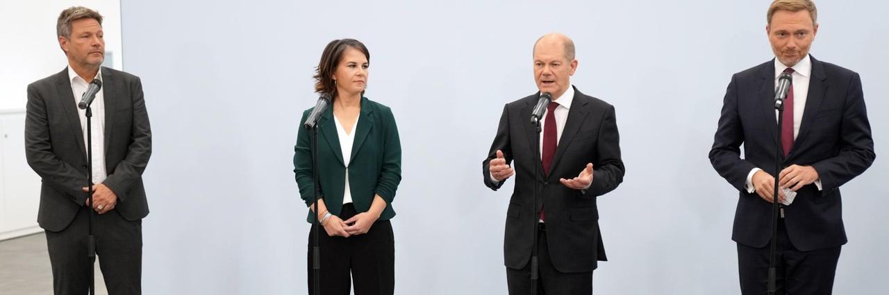 Wichtige Personen von den 3 Parteien stehen bei einer Presse-Konferenz an Mikrofonen.
