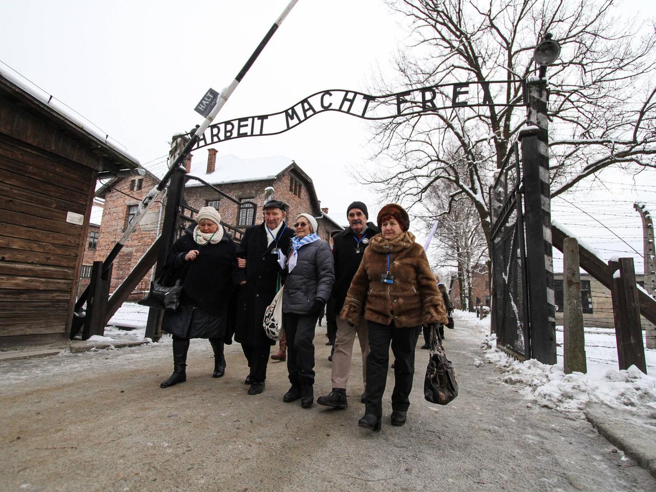 Überlebende des Konzentrationslagers Auschwitz vor dem Eingang mit dem Schriftzug "Arbeit macht frei".