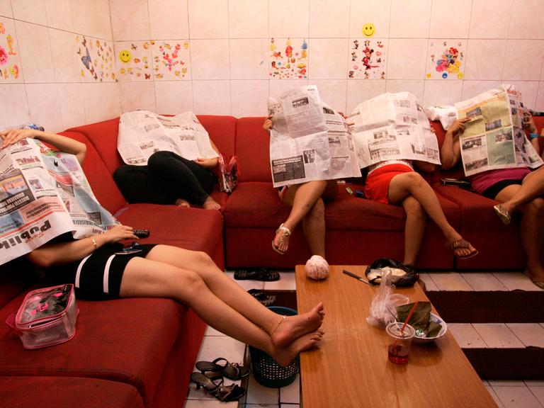 Indonesische Prostituierte sitzen in einem Hotel und verstecken ihre Köpfe hinter Zeitungen.