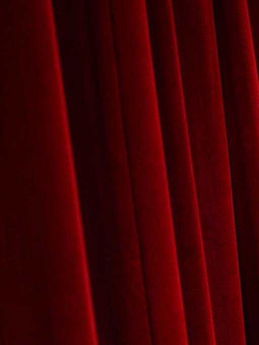 Blick auf einen schweren, roten, Falten werfenden Bühnenvorhang