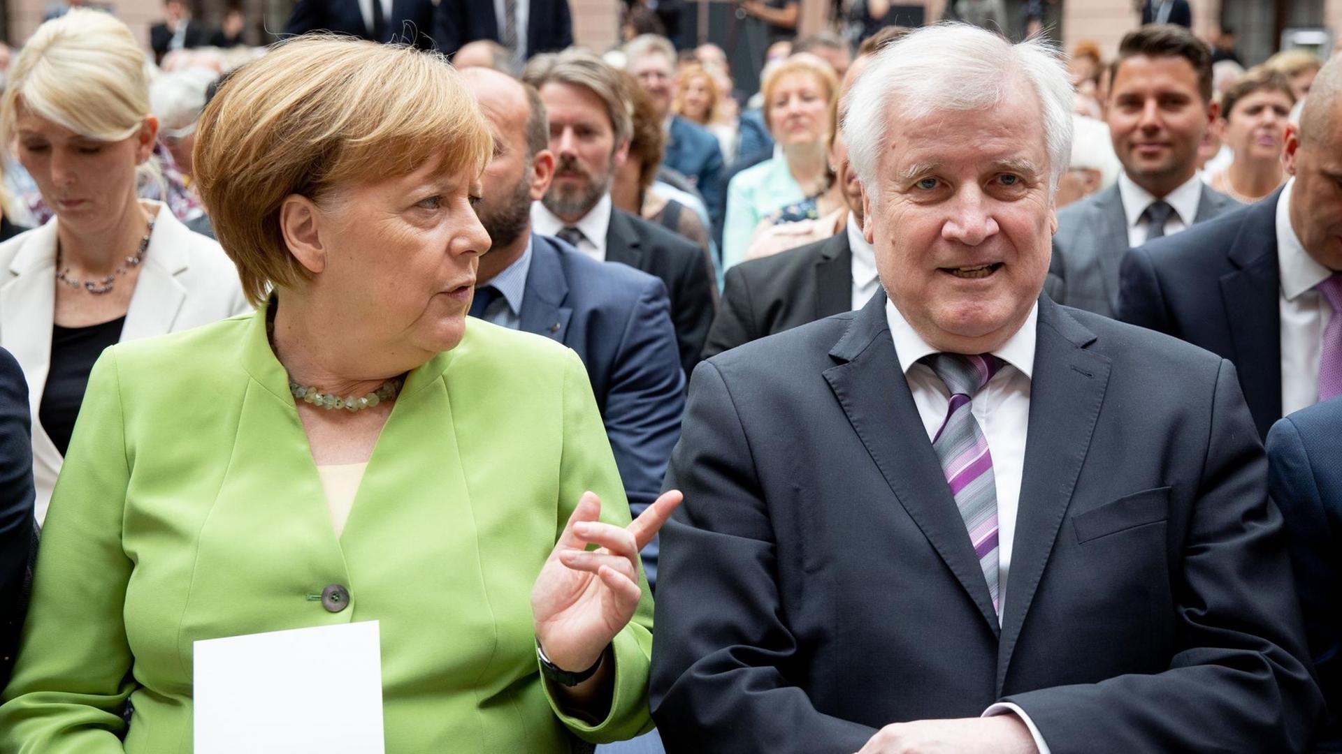 Merkel und Seehofer sitzen nebeneinander, Merkel spricht Seehofer an.