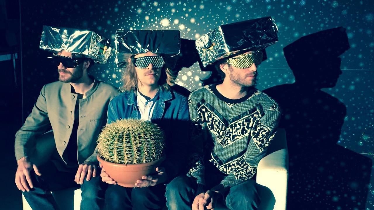 Das Trio Heinz Herbert sitzt mit einem Kaktus in der Hand vor einer Wand voller Sterne