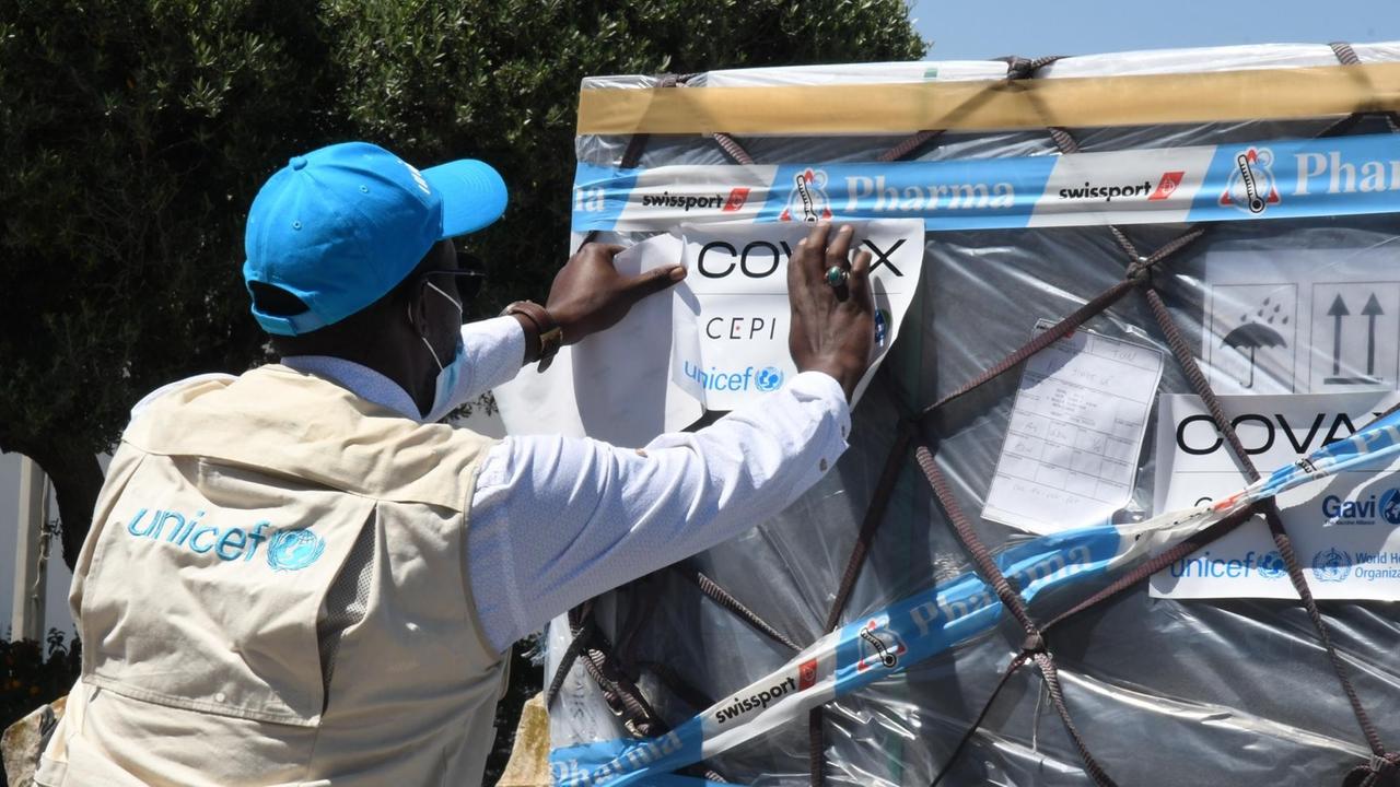 Ein Mitarbeiter der Vereinten Nationen überprüft eine neue Charge von Corona-Impfstoffen am Internationalen Flughafen Karthago und befestigt einen Zettel daran.