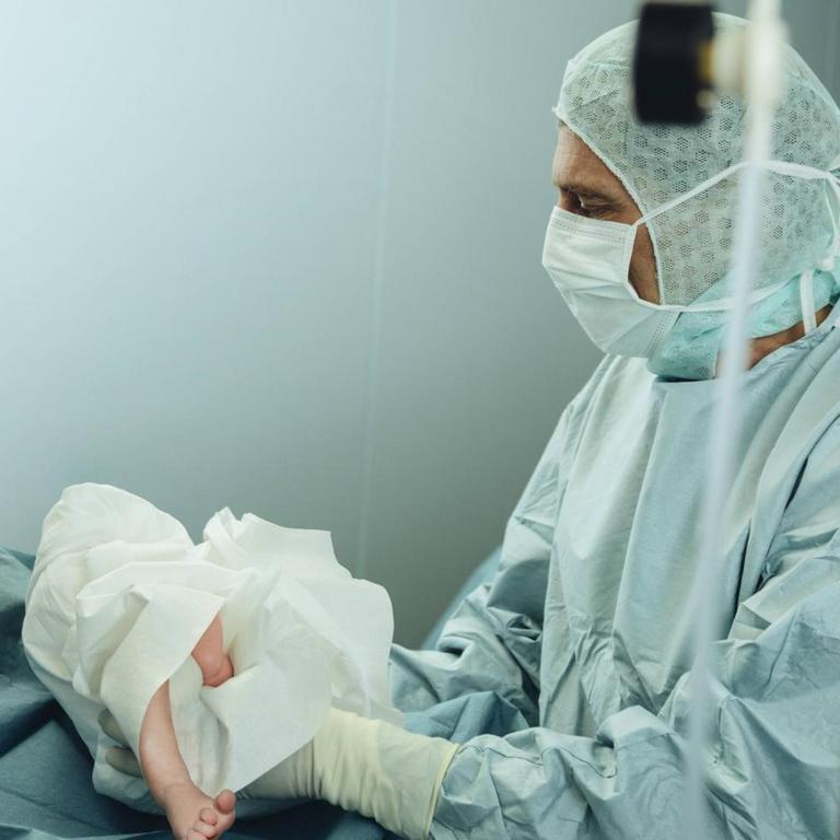 Ein Arzt hält in einem Kreißsaal ein neugeborenes Baby in den Händen (Symbolbild)