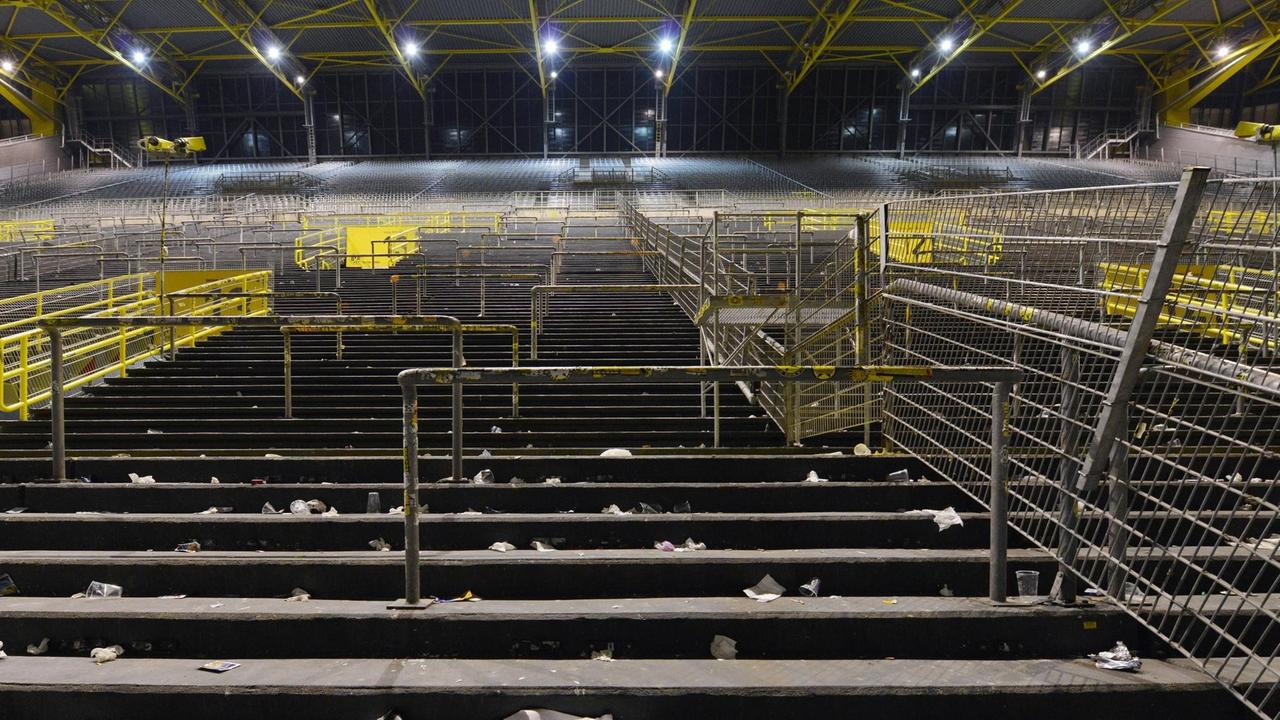 Die leere Südtribüne von unten nach einem Spiel fotografiert. Auf dem Boden liegen zertretene Bierbecher aus Plastik