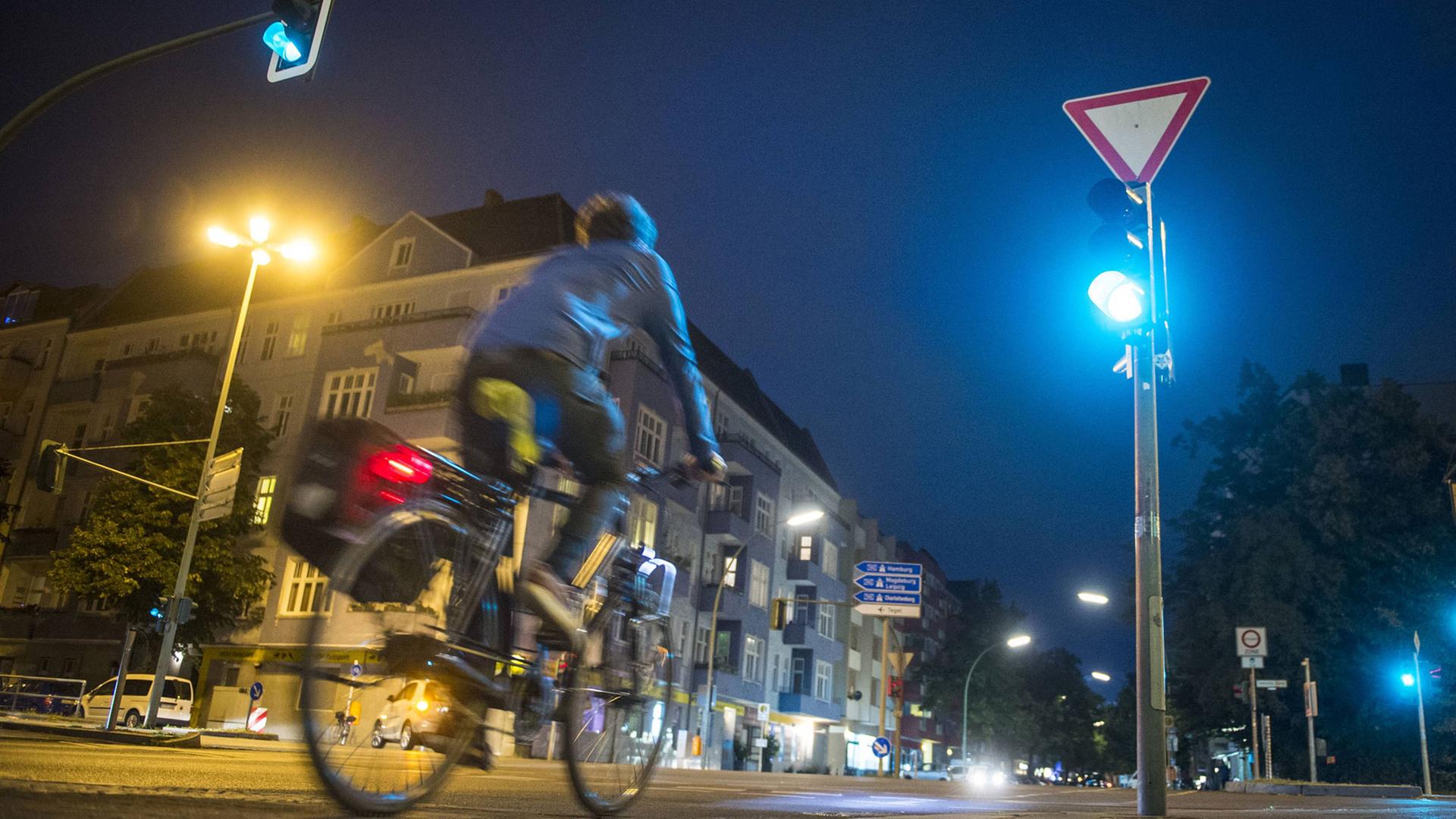 Ein Radfahrer fährt nachts über eine grüne Kreuzung.