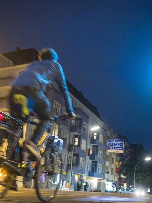 Ein Radfahrer fährt nachts über eine grüne Kreuzung.