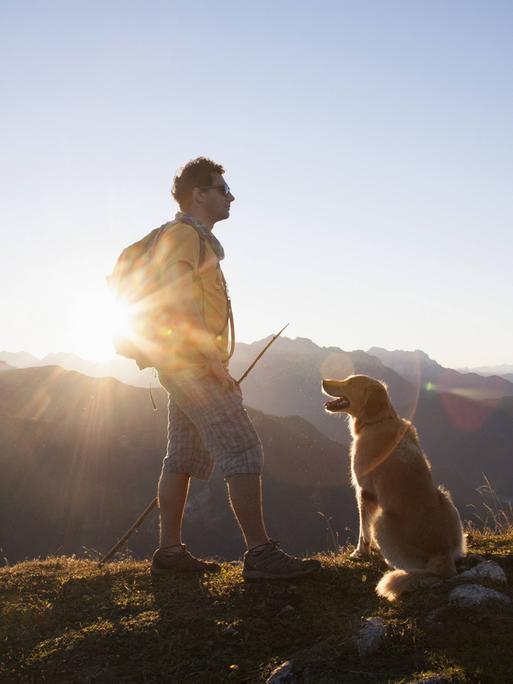 Ein Wanderer spaziert mit seinem Hund in den Bergen.