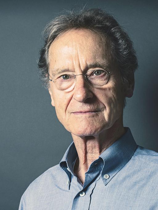 Bernhard Schlink steht vor einem blaugrauem Hintergrund und schaut in die Kamera.