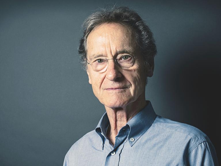 Bernhard Schlink steht vor einem blaugrauem Hintergrund und schaut in die Kamera.