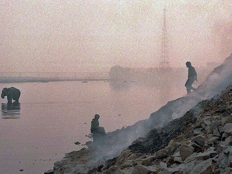 Zwei Männern und ein Elefant sind in der dunstigen Luft neben einem brennender Müllhalde am Yamuna Fluß in Neu Delhi nur als Umriss zu erkennen. Der heilige Yamuna Fluß ist stark durch industrielle Abwässer verschmutzt.