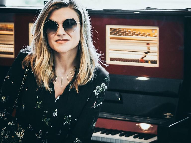 Melody Gardot sitzt mit dunkler Sonnenbrille vor einem alten Klavier.