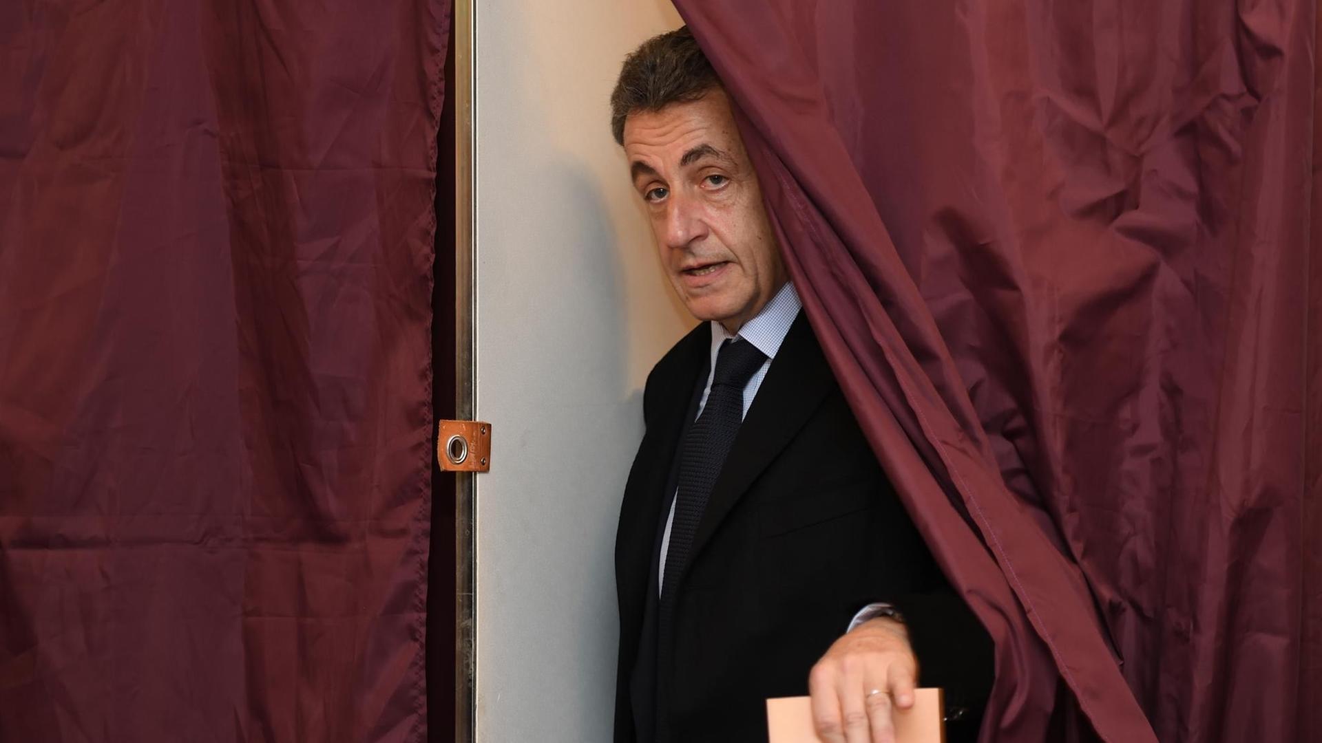 Frankreichs früherer Präsident Nicolas Sarkozy kommt mit einem Wahlzettel in der Hand aus der Kabine