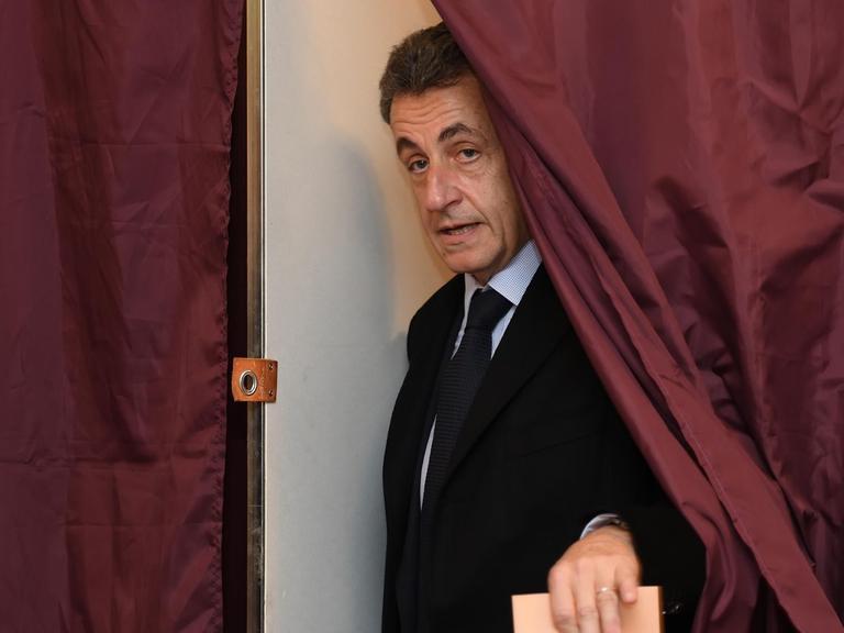 Frankreichs früherer Präsident Nicolas Sarkozy kommt mit einem Wahlzettel in der Hand aus der Kabine