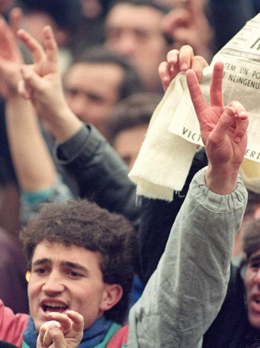 Tausende Rumänen jubeln am 24. Dezember 1989 in den Straßen von Bukarest. In der Zeitung ist zu lesen, dass Diktator Ceausescu und seine Frau verhaftet wurden.