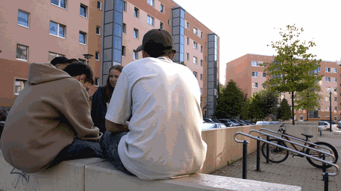 Jugendliche sitzen auf einer Mauer in einer Plattenbausiedlung