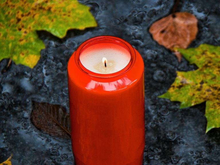 Ein Grablicht zu Allerheiligen im Herbst mit Blättern