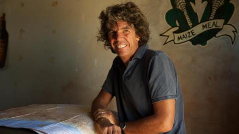 Wüstenfotograf Michael Martin lächelt braun gebrannt, auf dem Tisch neben ihm eine Landkarte