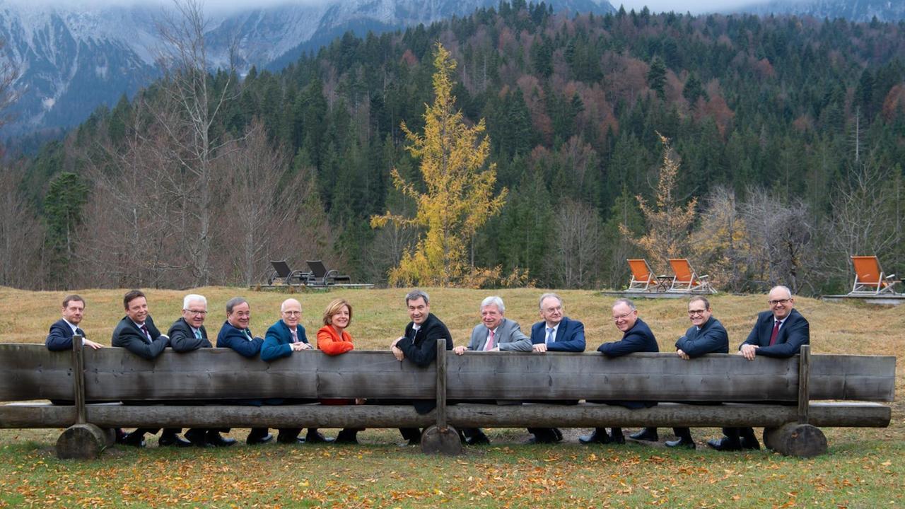 Die Ministerpräsidenten der Länder sitzen auf einer langen Holzbank und schauen in die Kamera
