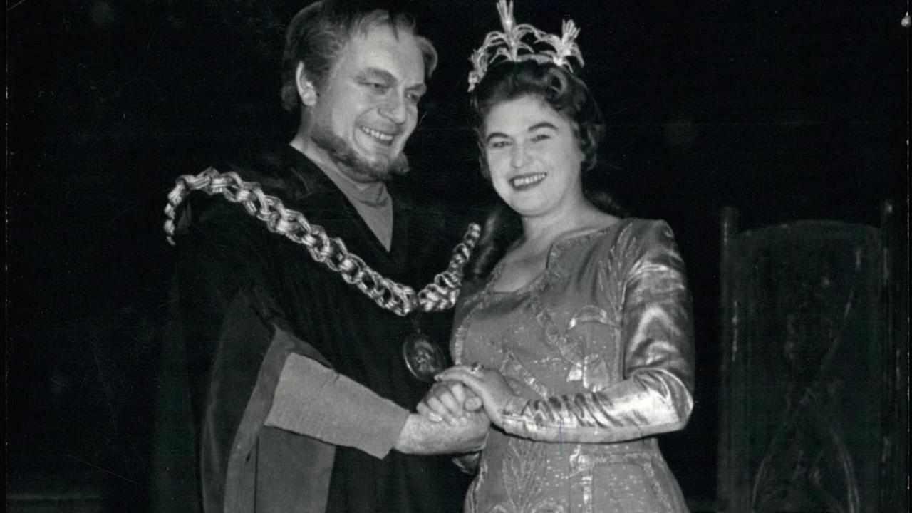 Schwarz-weiß-Foto mit einem Mann (links) und einer Frau: beide lächeln, tragen Kostüme und halten sich an den Händen. Sie trägt eine Krone auf dem Kopf.