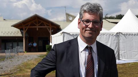 Anwalt Christof Wellens in Anzug, steht auf einer Wiese, im Hintergrund ein weißes Zelt.