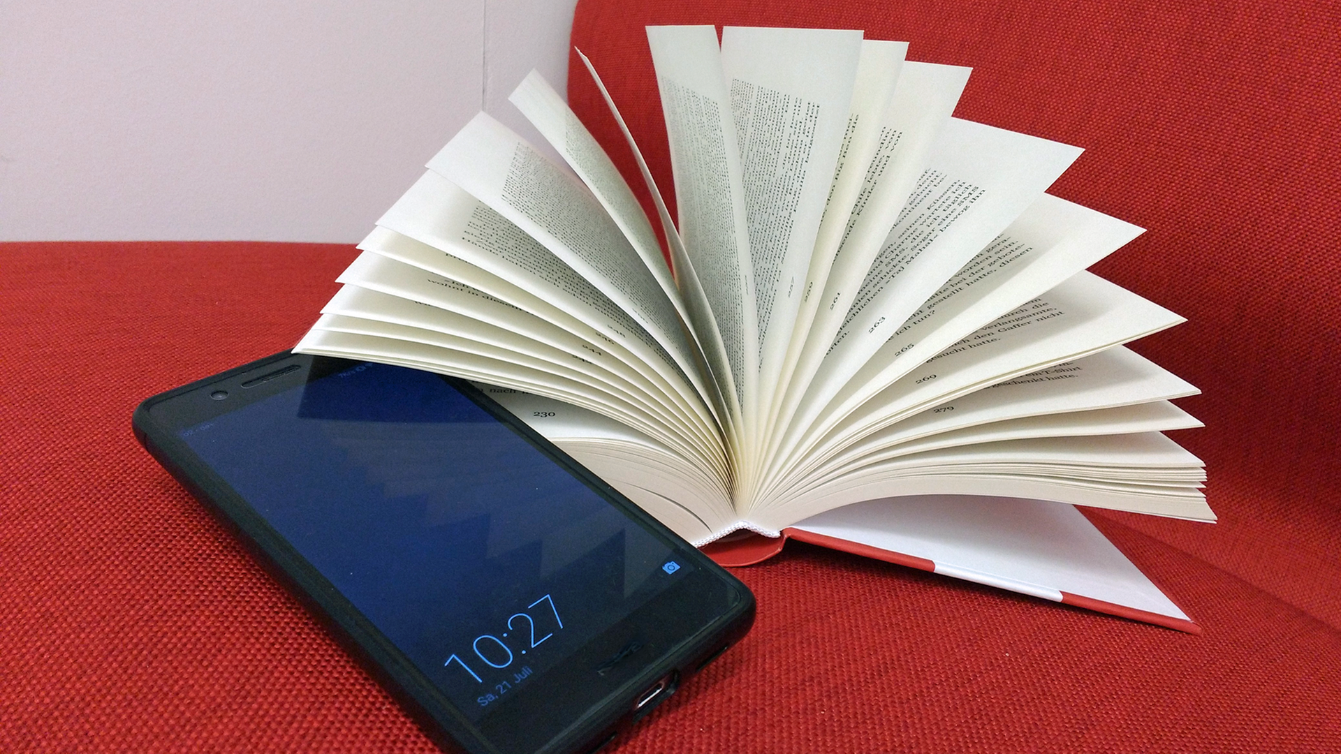 Ein Smartphone liegt neben einem aufgeschlagenen Buch