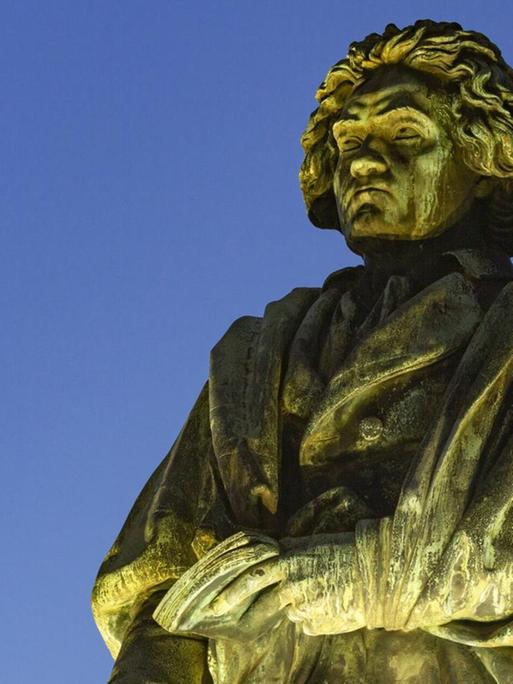 Denkmal am Münsterplatz in Bonn: der Komponist und Pianist Ludwig van Beethoven angestrahlt vor abendlichem Himmel.