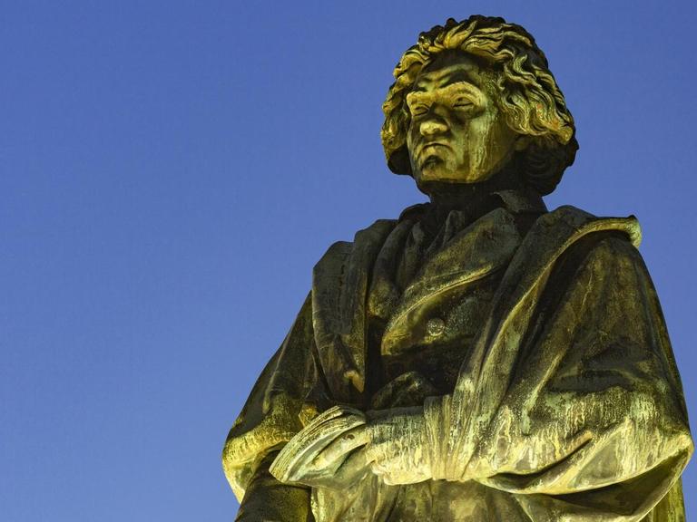 Denkmal am Münsterplatz in Bonn: der Komponist und Pianist Ludwig van Beethoven angestrahlt vor abendlichem Himmel.