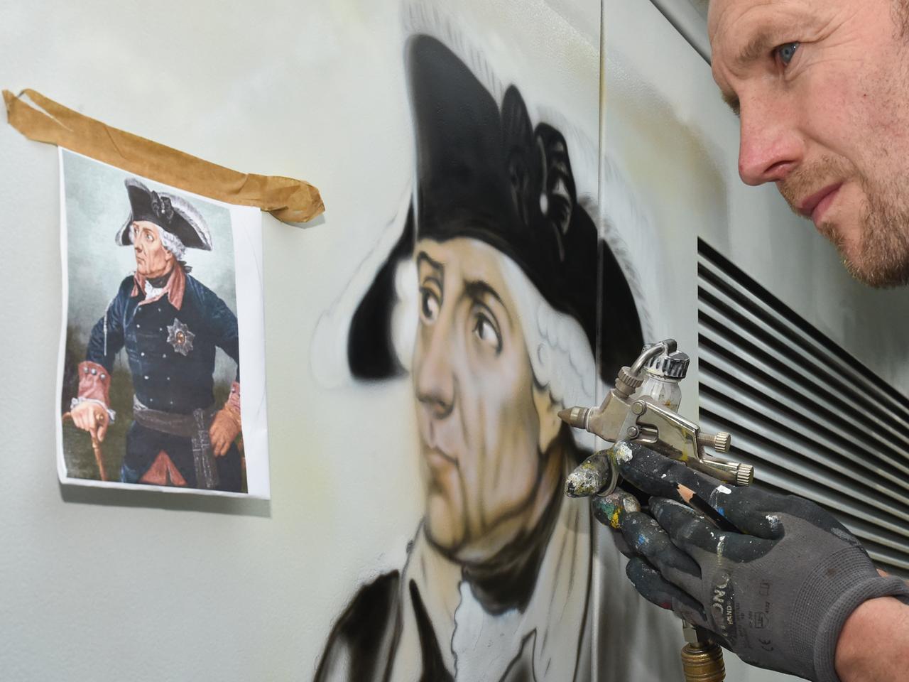Ein Airbrushmaler sprüht das Porträt von Friedrich II.
