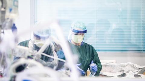 Zwei Krankenpfleger arbeiten in Schutzkleidung in einem Krankenzimmer auf der Intensivstation des Uniklinikums Essen, in dem ein Corona-Patient aus Frankreich behandelt wird.