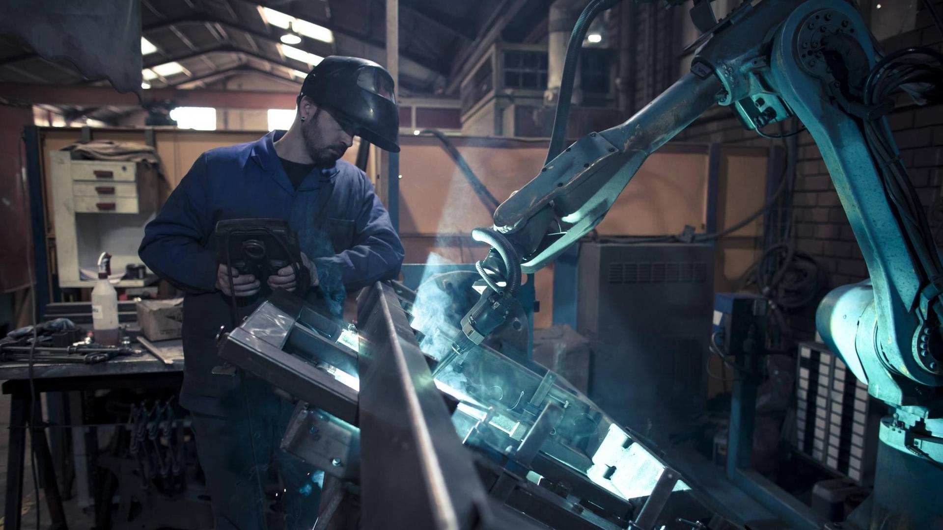 Ein Mann schweisst gemeinsam mit einem Roboter Metall (Symbolfoto).
