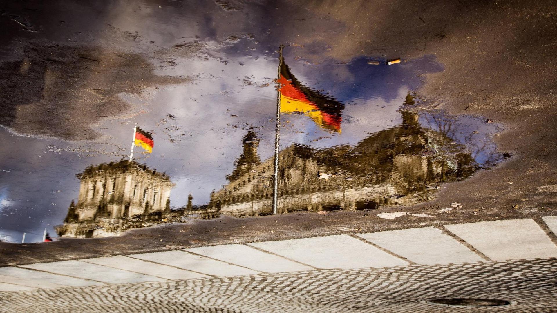 Das verzerrte Spiegelbild des Deutschen Bundestages in einer Pfütze. 