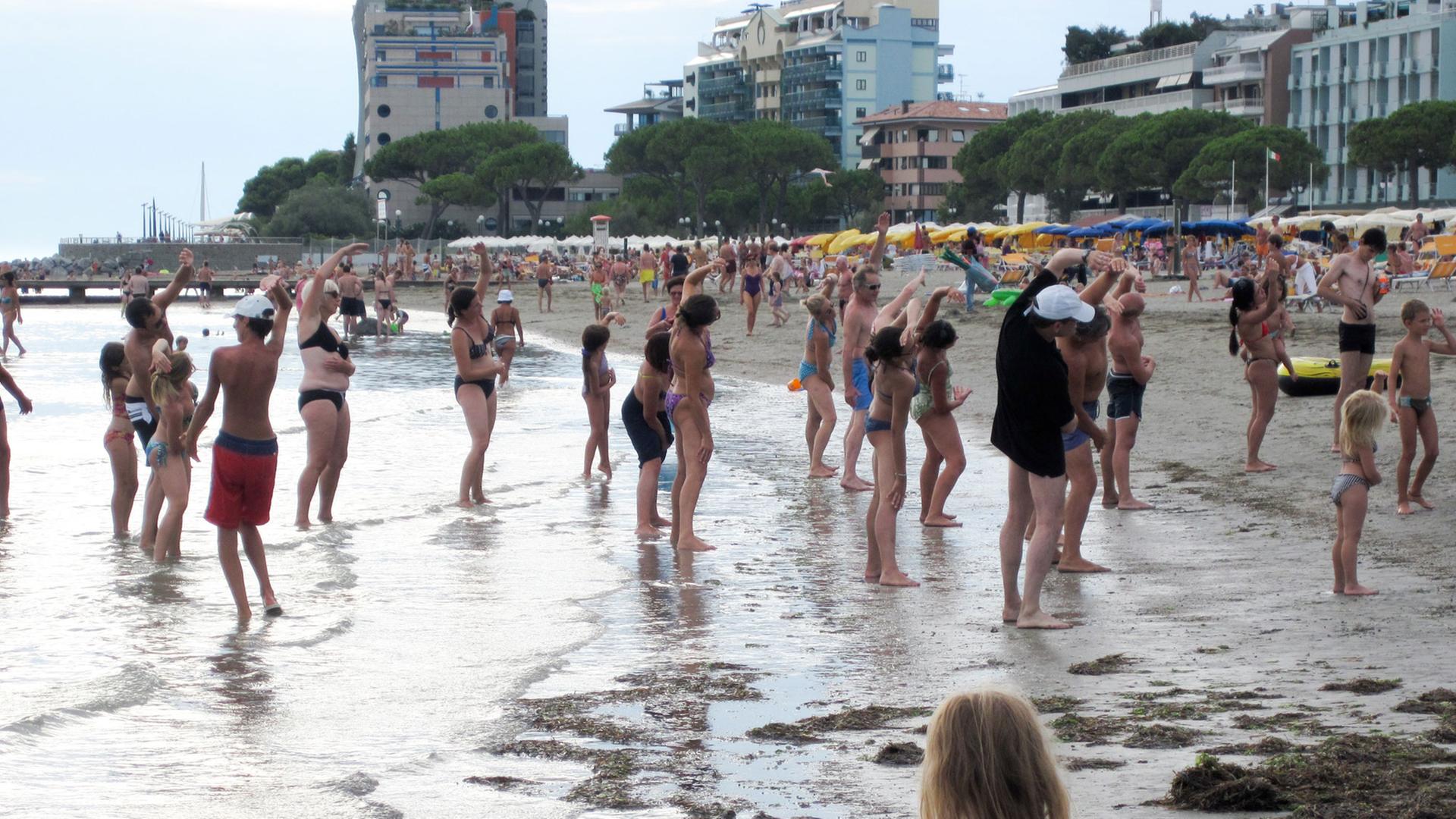 Urlauber machen Strandgymnastik an der Adria in Grado.