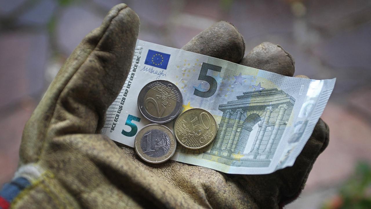 Ein Arbeitshandschuh in dem ein Fünf-Euro-Schein, eine Zwei-Euro-Münze, eine Ein-Euro-Münze sowie ein 50-Cent-Stück liegen.