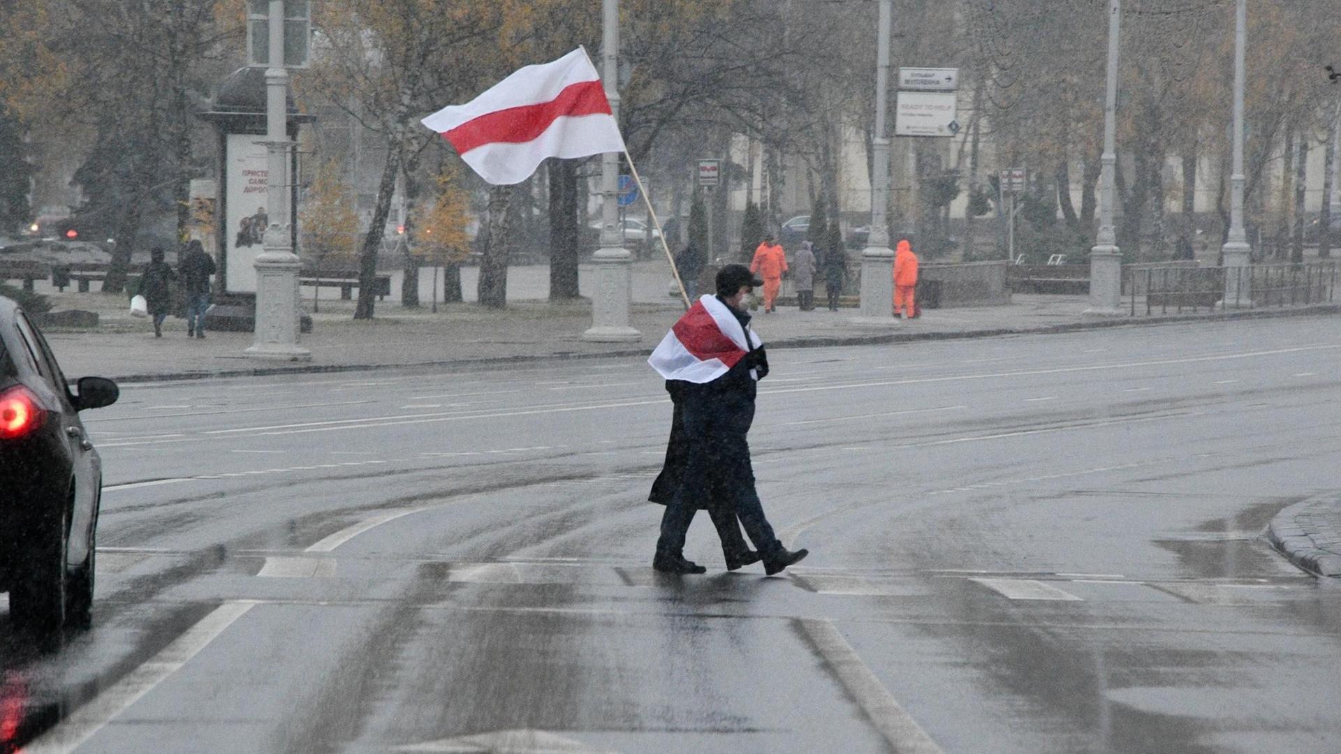 Ein Protestierender mit weiß-rot-weißer Fahne überquert eine Straße in Minsk.