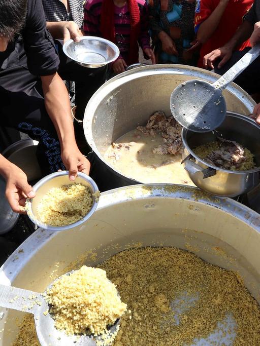 Zahlreiche Menschen stehen um zwei große Töpfe, aus denen Essen ausgegeben wird.