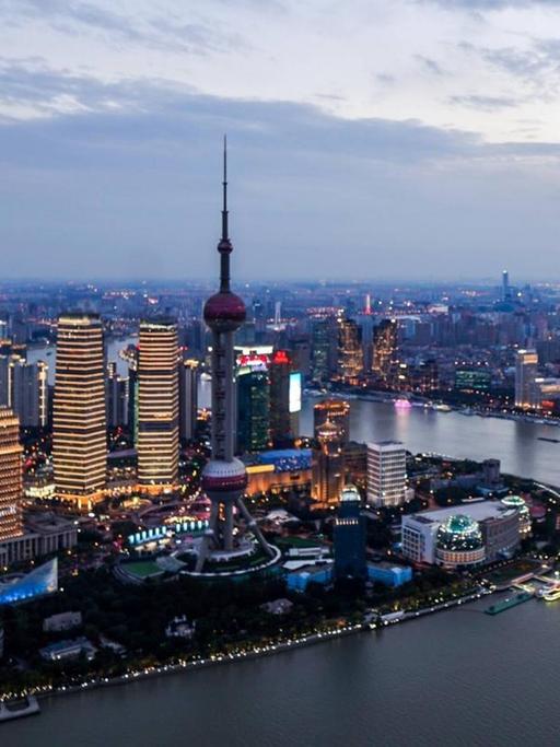 Abendaufnahme der beeindruckenden Skyline von Shanghai, wo zahlreiche Neonlichter leuchten.