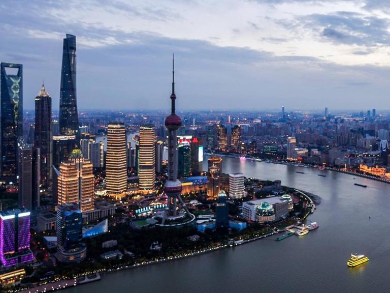 Abendaufnahme der beeindruckenden Skyline von Shanghai, wo zahlreiche Neonlichter leuchten.