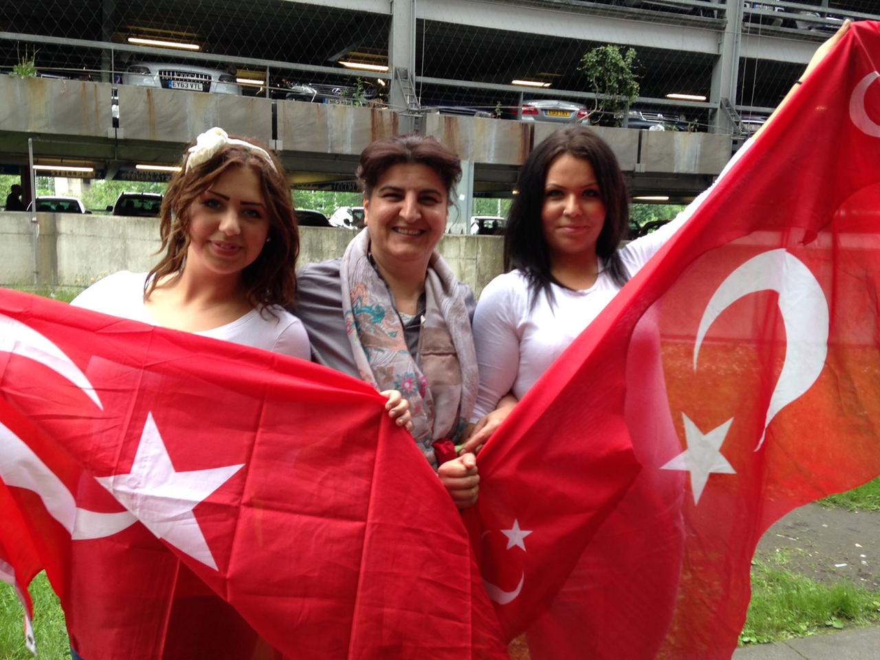 Drei Frauen halten vor der Lanxess-Arena türkische Flaggen hoch