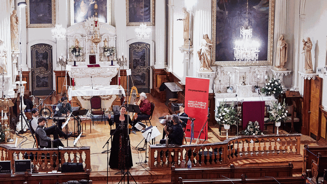 Eine Sängerin steht neben einigen Musikern im Altarraum einer hochbarocken Kirche, die viel goldnene Schmuck auf weißem Putz bietet.