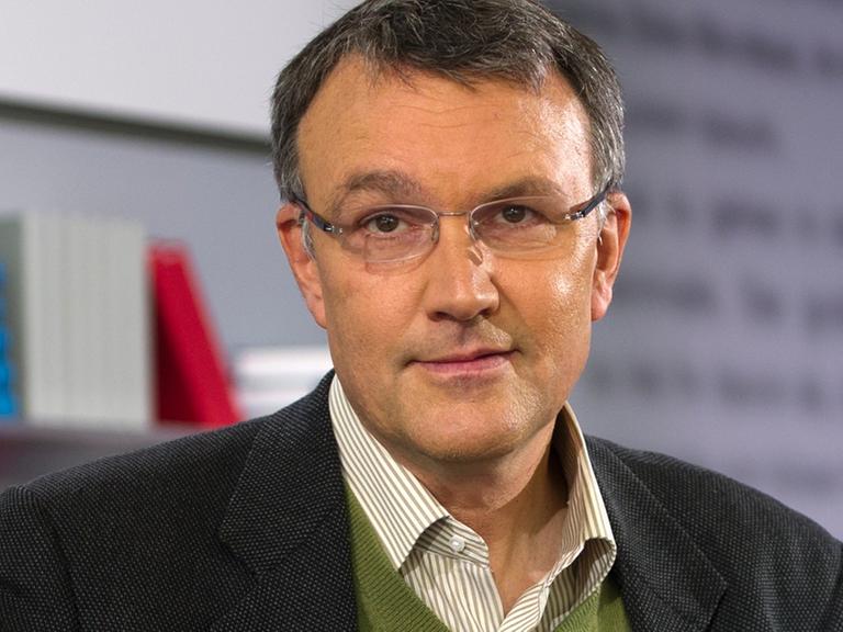 Lüders blickt freundlich in die Kamera, er trägt eine Brille. Hinter ihm sieht man ein Bücherregal.
