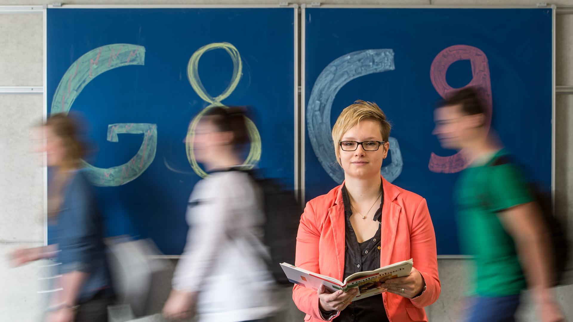 Gymnasiallehrerin Theresa Neudecker sitzt in einem Gymnasium in Straubing / Bayern vor einer Tafel mit der Aufschrift "G8" und "G9".