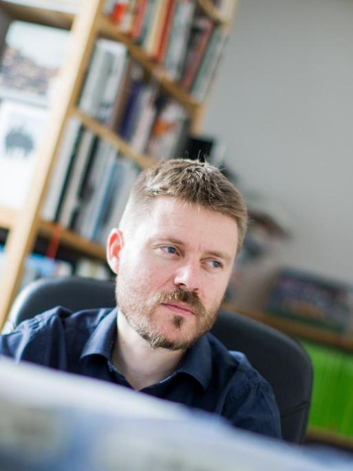 Ein Porträt des Fotojournalisten Christoph Bangert am Schreibtisch in einem Arbeitszimmer.