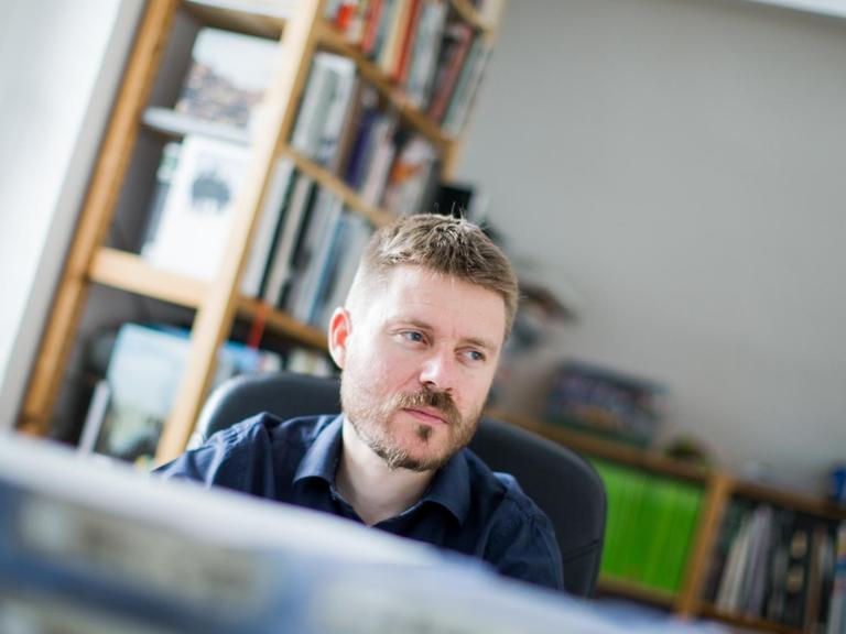Ein Porträt des Fotojournalisten Christoph Bangert am Schreibtisch in einem Arbeitszimmer.