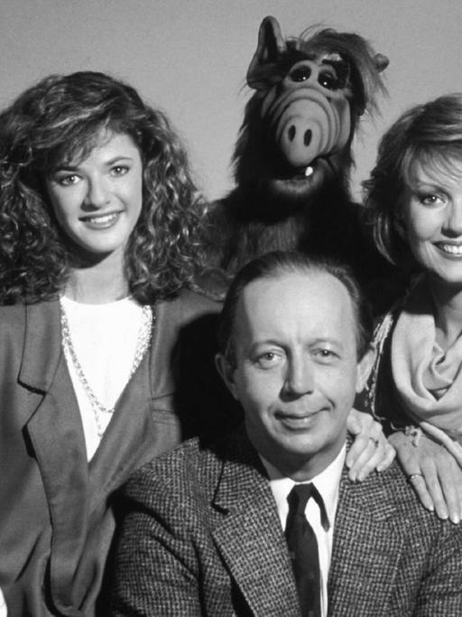 Grupppenbild der Familie mit Alf vor lila-grauem Hintergrund.
