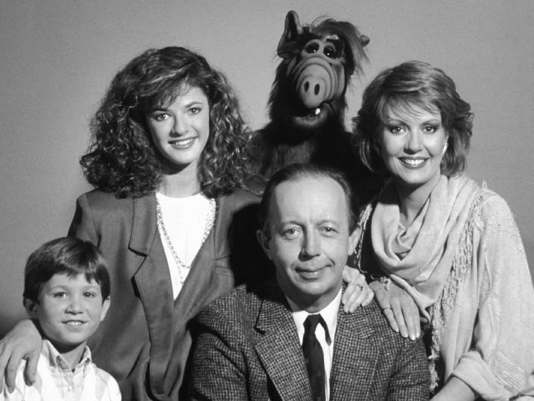 Grupppenbild der Familie mit Alf vor lila-grauem Hintergrund.
