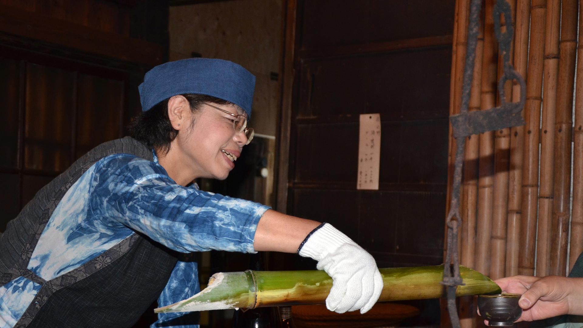 Eine japanische Frau schenkt mit einem Bambusrohr Sake ein