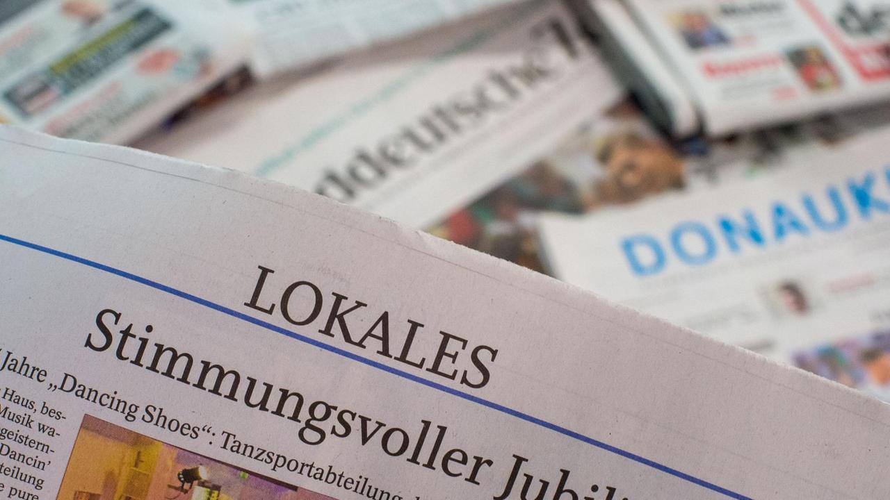 Eine Lokalzeitung wird über andere Zeitungen gehalten. Oben auf der Seite ist die Ressortbezeichnung "Lokales" zu lesen.